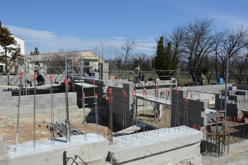 Home Sunlit construction site with workers on concrete foundation under a clear blue sky.